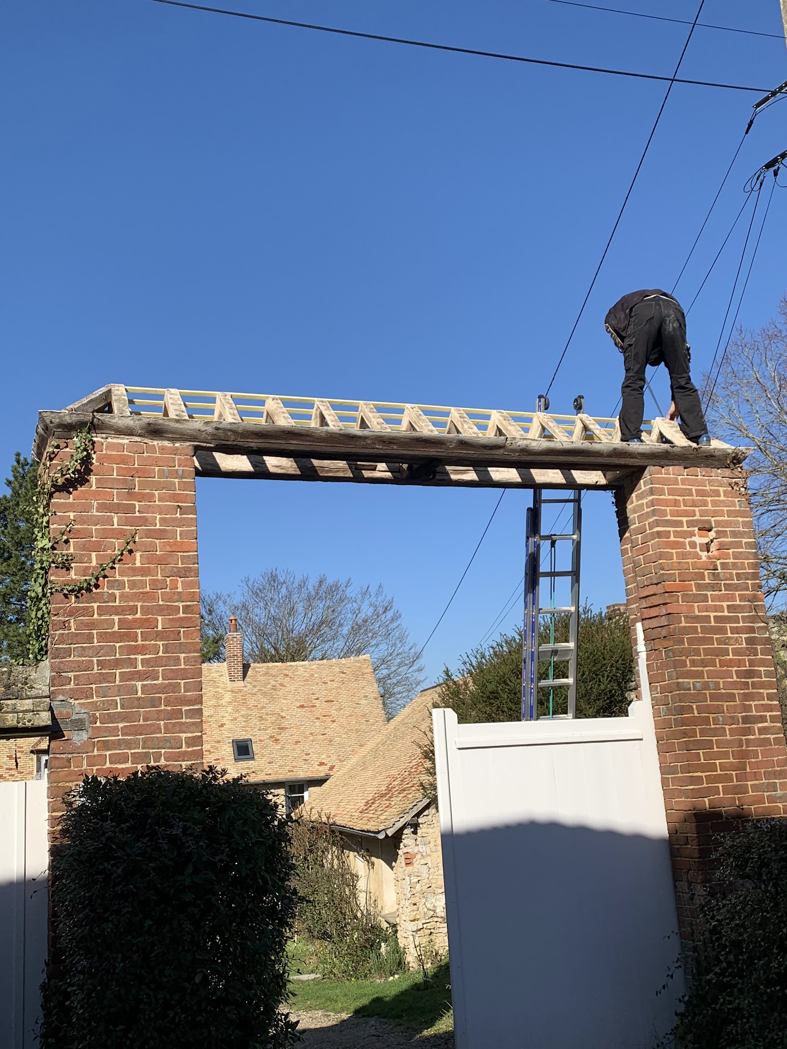 Installation d’une structure de toiture sur un portail en briques.